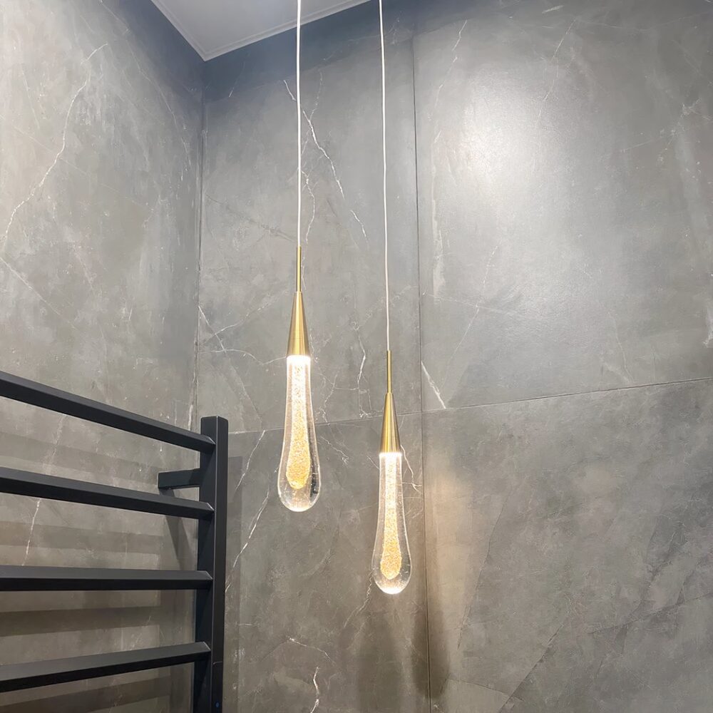 Lustre en forme de goutte d'eau suspendu au plafond, dans une pièce aux murs gris.