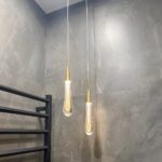 Lustre en forme de goutte d'eau suspendu au plafond, dans une pièce aux murs gris.
