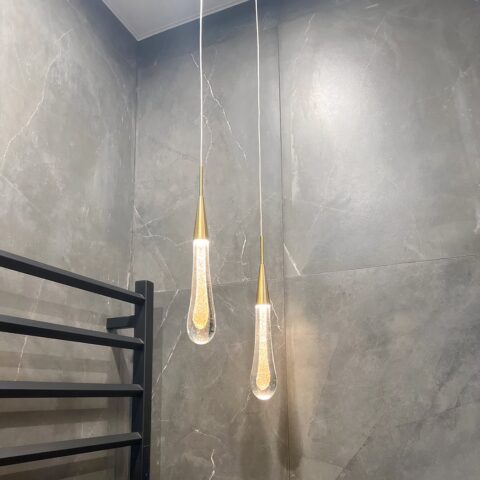 Lustre en forme de goutte d'eau suspendu au plafond, dans une pièce aux murs gris.