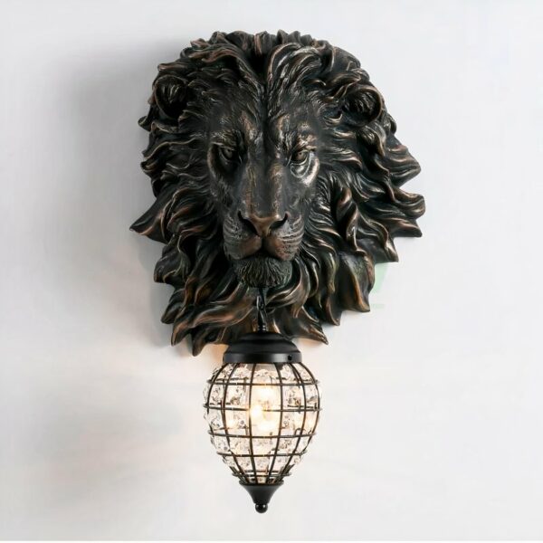 Applique murale en forme de tête de lion en résine noire. Sous sa gueule, une lanterne en forme de goutte en métal noir grillagé. Des imitations de diamants tout autour de la lanterne et une ampoule au centre allumée.