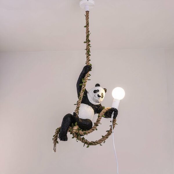 Suspension avec corde en chanvre entrelacée de feuillage. Un panda est accroché par sa patte avant droite, la corde passe dans ses pattes arrières et il tient une ampoule allumée dans sa patte avant gauche avec une partie de la corde.