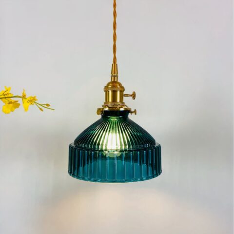 Suspension vintage avec câble torsadé doré et douille dorée, abat-jour bleu canard ressemblant à une cloche avec stries sur tout le tour. Ampoule allumée. Fleurs jaunes à gauche.