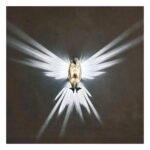 on voit sur un fond noir une applique murale allumée qui fait des ailes d'oiseaux sur les murs avec sa lumière