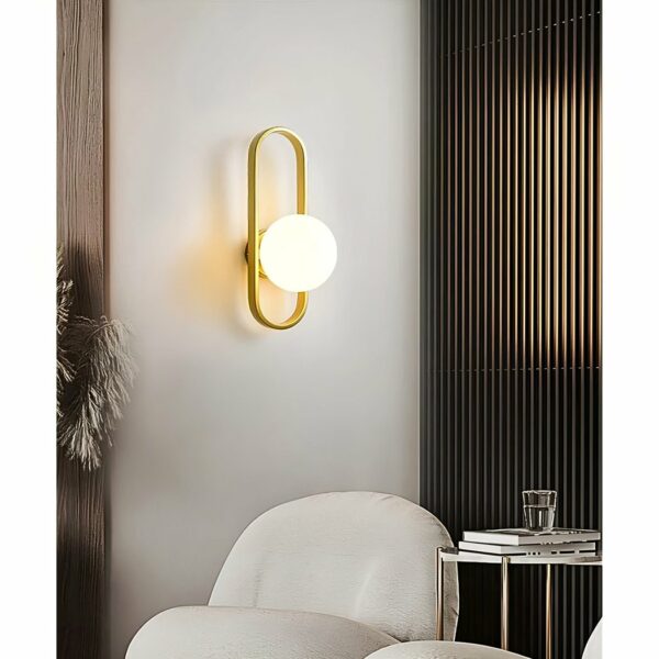 on voit dan sun salon avec un fauteuil blanc une applique murale moderne dorée avec une boule