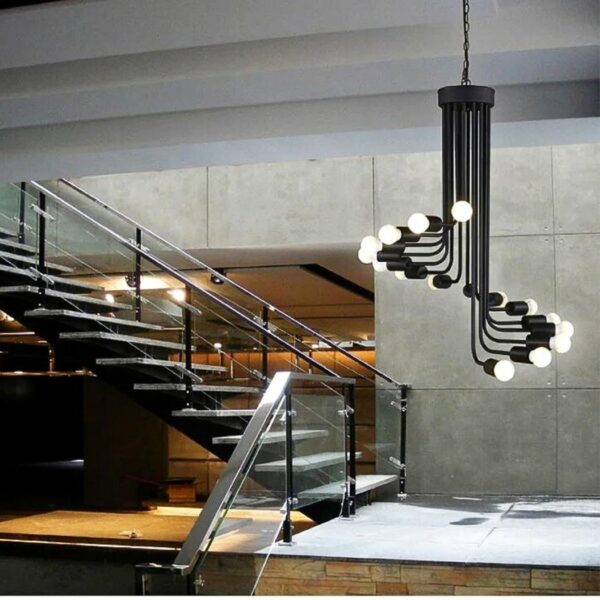 on voit dans un salon avec des escaliers dans le fond un lustre en fer forgé noir avec des ampoules apparentes