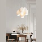 Suspension multiple cinq abat-jour en céramique blanche mis en scene au dessus d'une table de salle à manger décorée d'un bonsaï et sur fond gris.