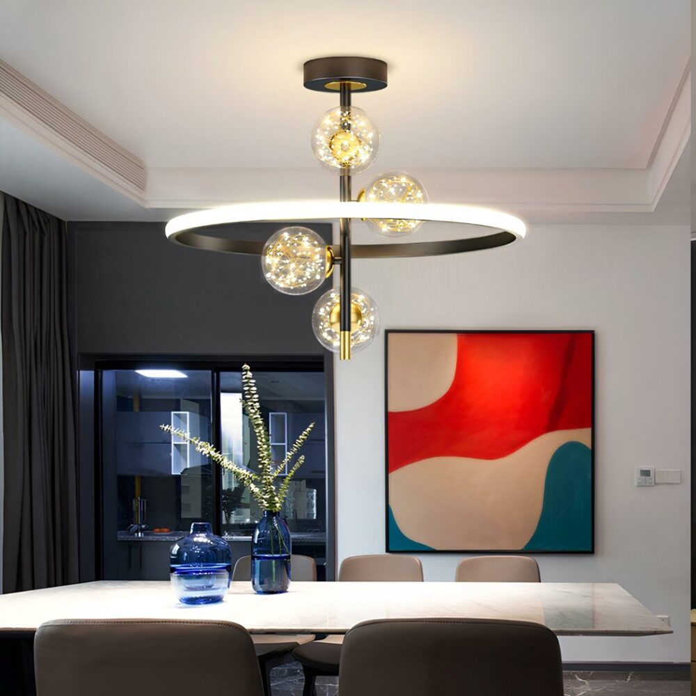 Lustre avec support rond noir au plafond, une verticale noire fixée dessus. 4 boules transparentes avec fils dorées à l'intérieur et diodes de lumière donnant l'impression que ça scintille. L'ensemble est entouré d'un cercle lumineux à l'extérieur et noir à l'intérieur. Fixé au-dessus d'une table rectangulaire blanche avec 5 chaises grises autour. 2 vases bleus sur la table remplis d'eau dont un à des fleurs longues. Sur le mur en face, un cadre abstrait beige, rouge et bleu. A gauche une baie vitrée avec mur gris, encadrement noir et rideau gris.