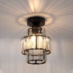 Lustre plafonnier de forme cylindrique avec 3 rangées de lamelles style cristal. Le support u plafond est de couleur noire et les lamelles sont fixées sur des cercles noirs. Les ampoules sont allumées et diffusent des rayons au plafond autour du lustre.