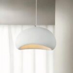 Lustre blanc en forme de dôme tenu par un câble blanc. En arrière-plan, un mur beige avec une fenêtre.