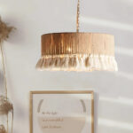 Lustre bohème en rotin avec pampilles en tissu de forme circulaire. Au fond, un mur blanc avec un cadre.