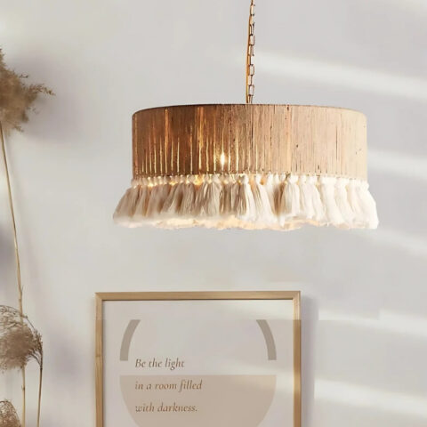 Lustre bohème en rotin avec pampilles en tissu de forme circulaire. Au fond, un mur blanc avec un cadre.