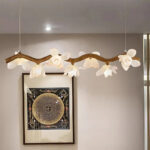 Lustre en résine imitation bois flotté avec fleurs allumé et fixé face à un mur beige avec un cadre au motif asiatique.