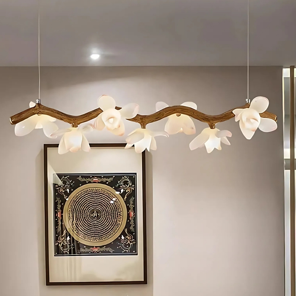 Lustre en résine imitation bois flotté avec fleurs allumé et fixé face à un mur beige avec un cadre au motif asiatique.