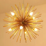 Lustre spoutink doré avec plusieurs ampoules allumées sur fond marron clair.