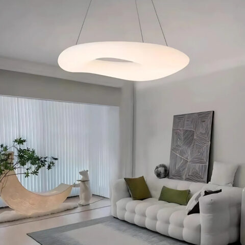 Lustre suspendu anneau lumineux allumé fixé dans un salon avec une grand fenêtre sur la gauche et un canapé sur la droite de couleur grise avec un tableau au-dessus.