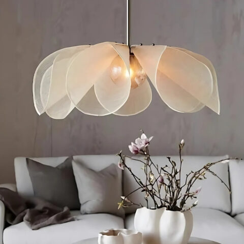 Lustre suspendu en forme de fleur en tissu blanc allumé au-dessus d'une table basse avec des fleurs et un canapé gris en arrière plan.