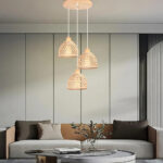 Suspension 3 lampes en rotin et bambou allumée et fixée dans un salon au-dessus d'une table basse. Derrière, un canapé gris et marron avec des coussins assortis contre un mur blanc.