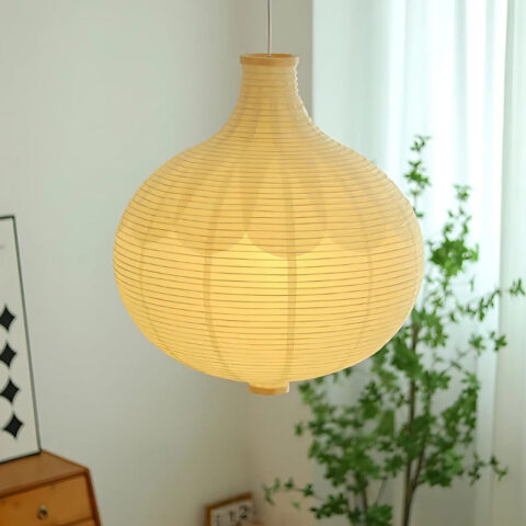 Suspension élégante en papier japonais allumée dans un salon. Une plante verte derrière et à gauche, un meuble marron.