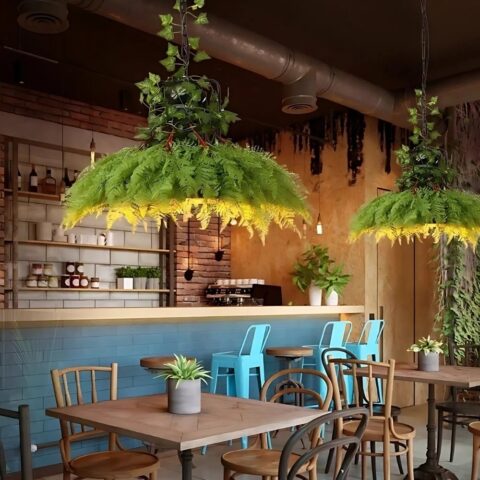 Suspension jungle avec feuillage suspendue au-dessus d'une table dans un établissement tel qu'un restaurant. La suspension est allumée et de forme ronde. La table en-dessous est carrée et en bois avec deux chaises autour. En arrière plan, un conmptoir de bar.