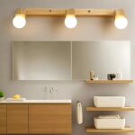 Applique murale en bois et métal avec trois lumières rondes, idéale pour éclairer une salle de bain de manière moderne et chaleureuse.