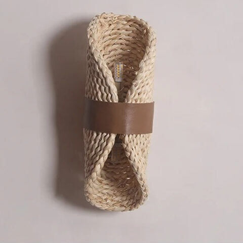 Applique murale en rotin style japandi beige de forme circulaire enroulé et maintenu par un cerclage en cuire PU marron sur fond uni
