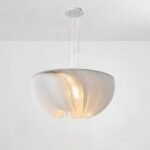 lustre blanc en forme de coque plissée, suspendu au plafond avec trois fils, diffusant une lumière douce et chaleureuse, sur fond neutre.