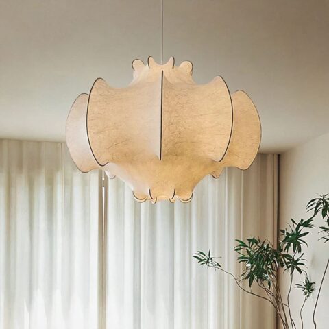 Suspension lumineuse aux courbes organiques, en soie texturée blanche, suspendue au-dessus d'un plafond devant des rideaux clairs.