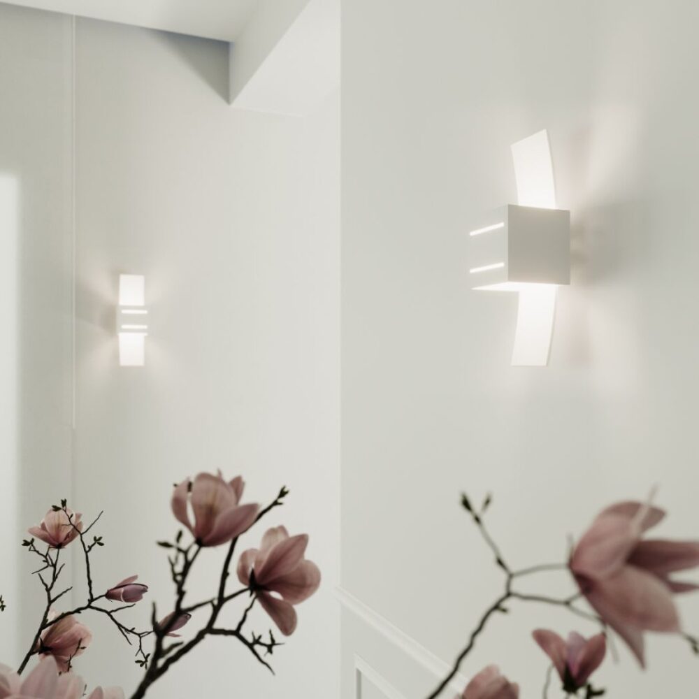 Deux appliques blanches à ailes en verre reflétées dans un miroir près de fleurs