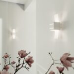 Deux appliques blanches à ailes en verre reflétées dans un miroir près de fleurs