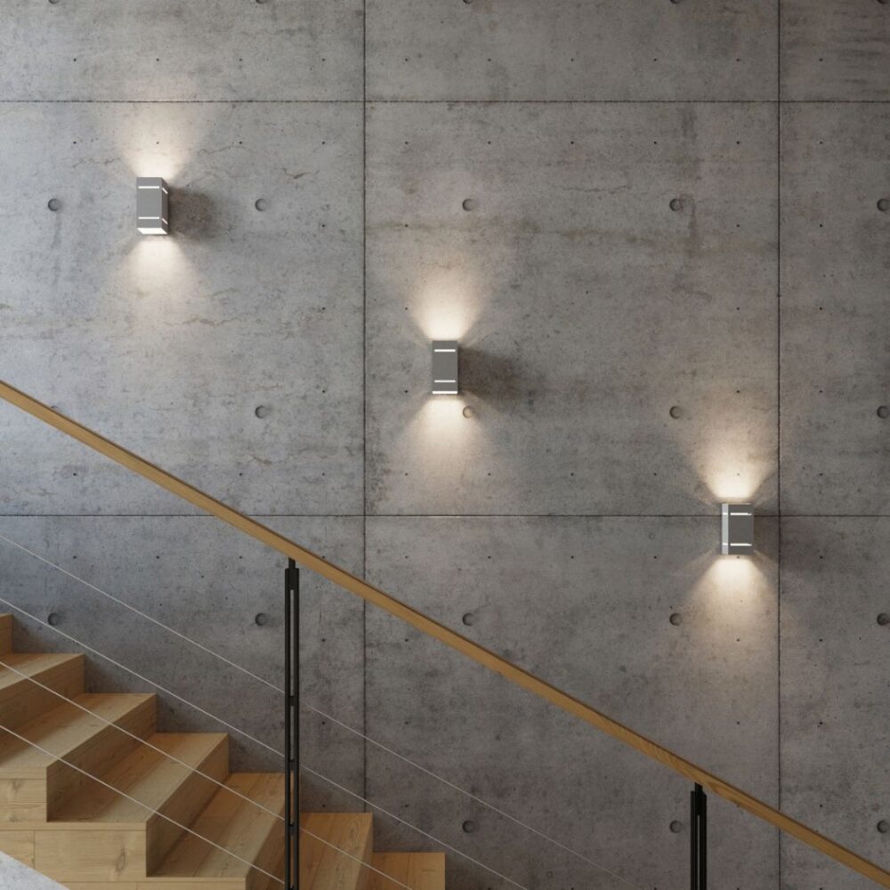 Trois petites appliques en aluminium projetant la lumière vers le haut et le bas sur un mur en béton