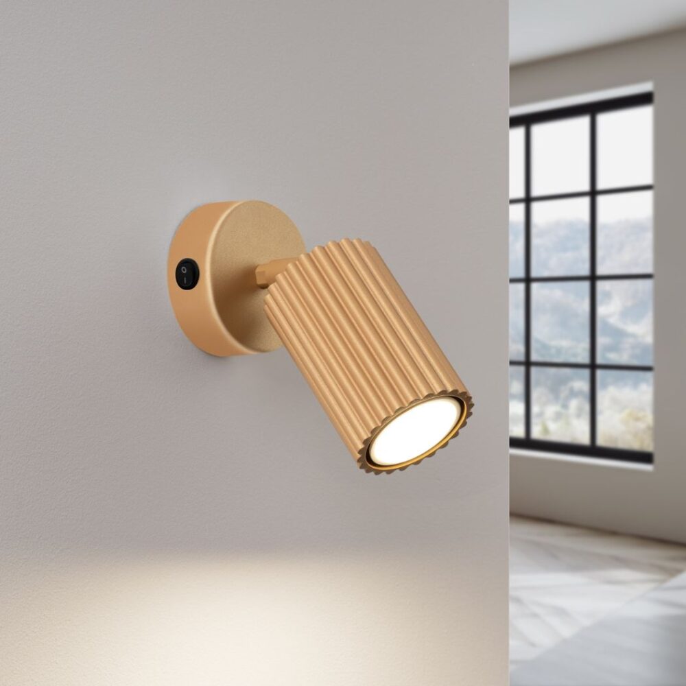Applique murale spot orientable façon liseuse en métal doré nervuré sur un mur blanc
