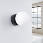 Applique murale ronde et minimaliste en forme de globe en métal noir et verre sur un mur blanc