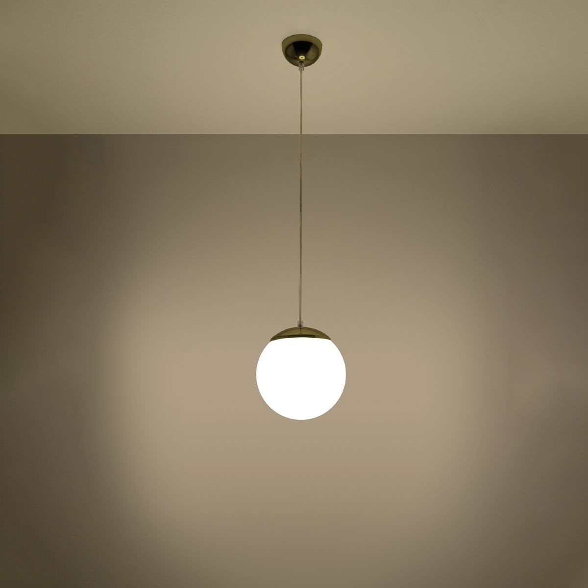 Suspension globe en verre blanc à culot doré allumée sur mur beige