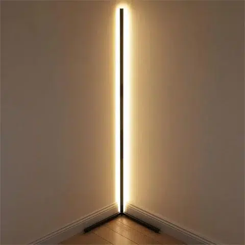 Lampadaire d’angle LED intelligent connecté, design minimaliste noir, lumière RGB personnalisable, installé dans l'angle d'une chambre face à un mur, réfléchissant ainsi son halo de lumière.