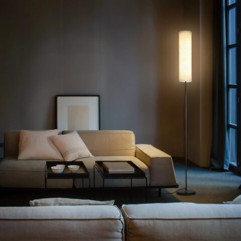 Lampadaire LED d’angle télécommandé à intensité variable au design moderne en métal noir et tissu beige dans le coin d'un salon moderne.