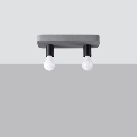 Plafonnier rectangulaire en béton gris fixé au plafond. Deux ampoules blanches de forme classique pendent vers le bas, chacune insérée dans une douille cylindrique noire. L’ensemble a un style très simple et minimaliste, avec un côté brut et industriel. L’arrière-plan est neutre, gris clair, ce qui met en valeur la sobriété du luminaire.
