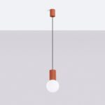 Suspension minimaliste design aux teintes vibrantes en aluminium et verre opalin, ici le modele terracotta suspendu à un plafond blanc et un fond gris.