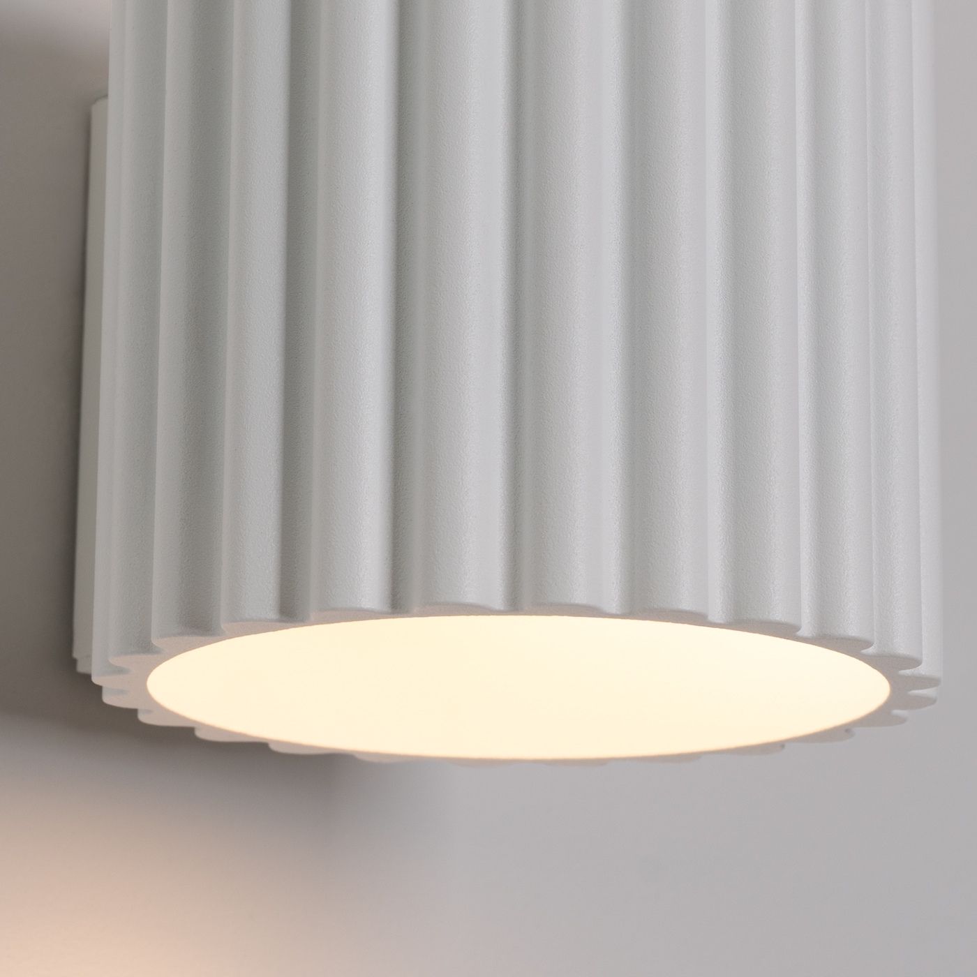 Gros plan de l'applique blanche cannelée avec sa lueur chaude vers le bas