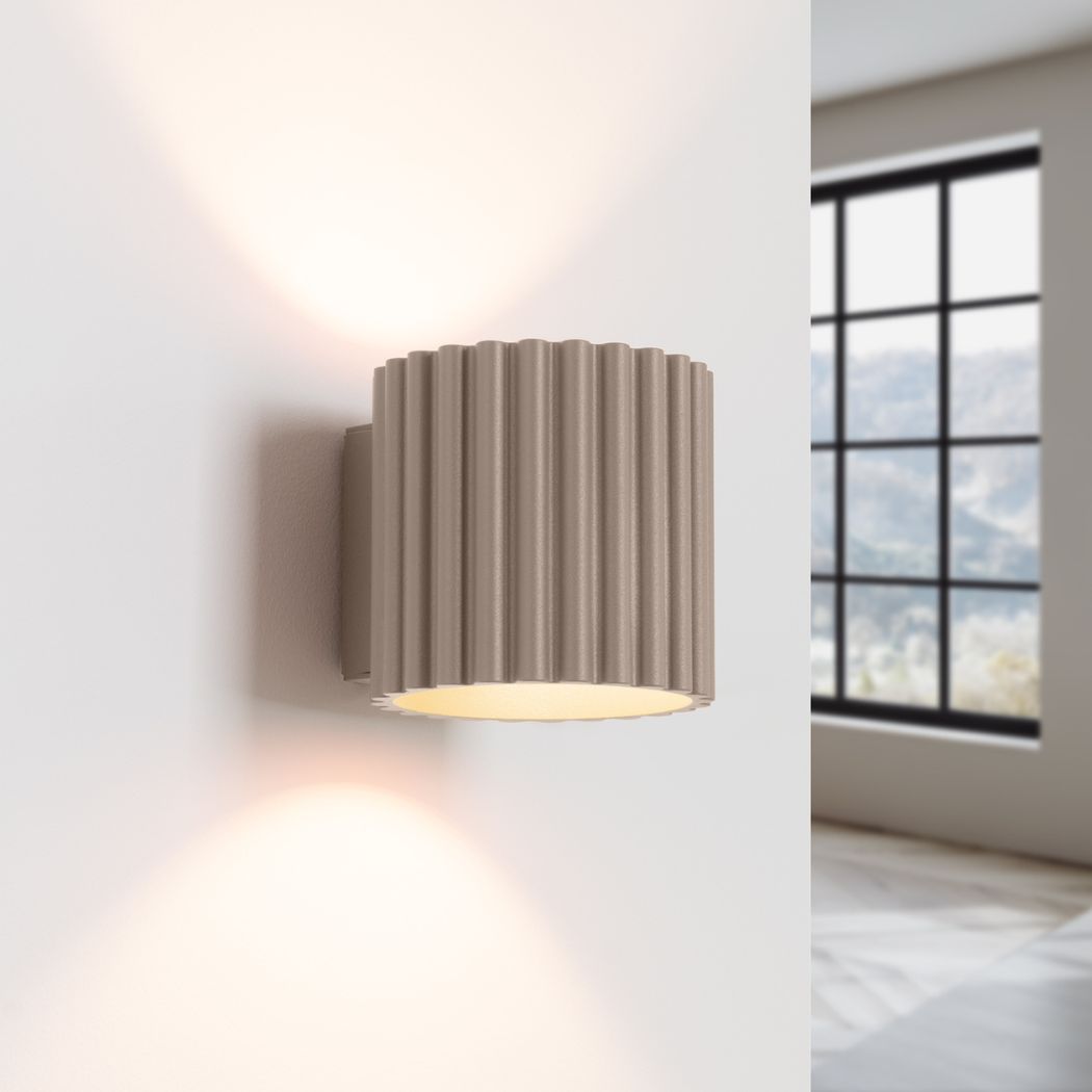 Applique murale ronde et texturée dans un coloris taupe, avec en fond un mur blanc et une fenêtre