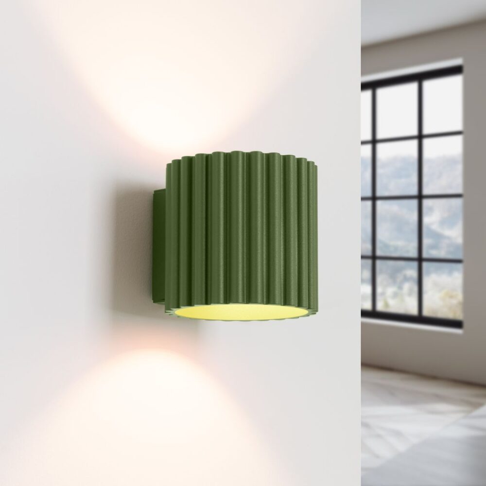 Applique murale vert olive de forme cylindrique et texturée, sur un mur blanc avec une fenêtre en fond