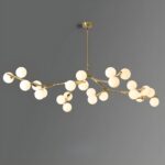 Lustre doré allumé, avec des petites boules en verre au bout de chaque branche, sur fond gris.