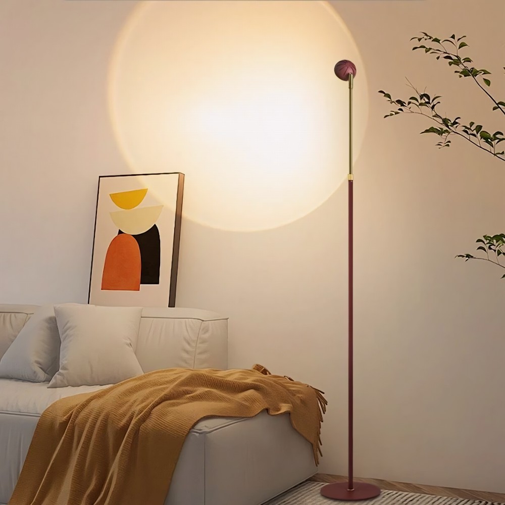 Salon cosy éclairé par un lampadaire sunset projection au design minimaliste diffusant un large halo lumineux rond sur le mur, canapé blanc, plaid ocre, tableau abstrait moderne et plante verte décorative.