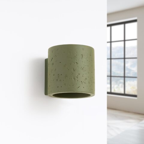Applique murale cylindrique en béton vert olive avec texture brute naturelle fixée sur mur blanc dans intérieur moderne lumineux avec fenêtre industrielle.
