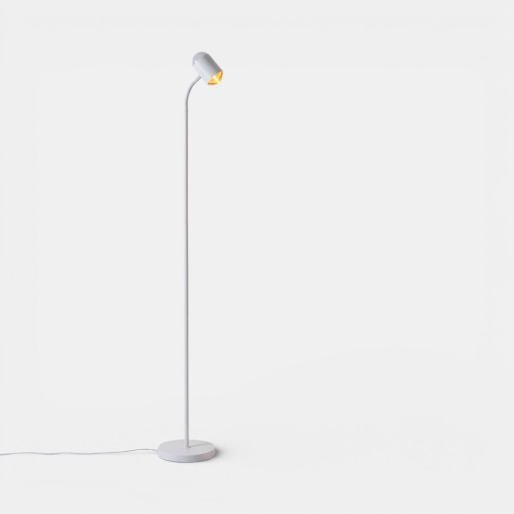 Lampadaire Halo sunset RGB avec télécommande : lampe blanche fine sur pied, tête inclinée diffusant une lumière chaude, posé sur un sol blanc épuré.