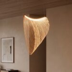 Notre suspension LED en bois design nid hirondelle aux lamelles courbes dorées rétroéclairées, suspendue dans un salon beige aux murs texturés et plafond bois.