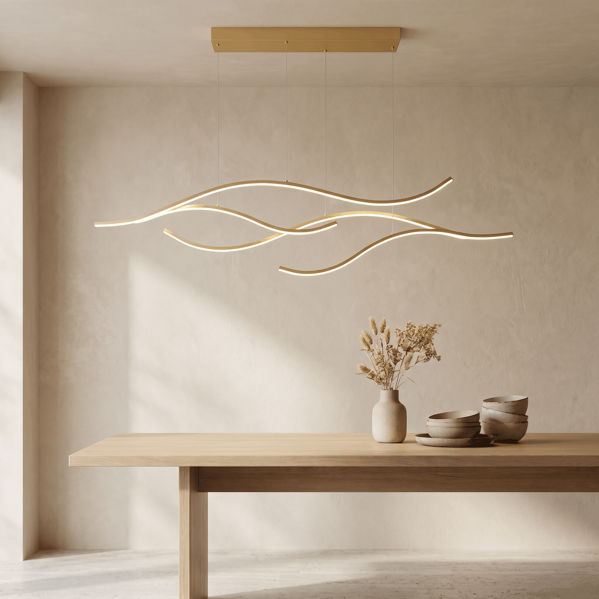 Une Suspension Plafonnier LED Design Vague Minimaliste en forme de lignes ondulées dorées, suspendue au plafond au-dessus d’une table en bois, dans une pièce claire au style épuré.