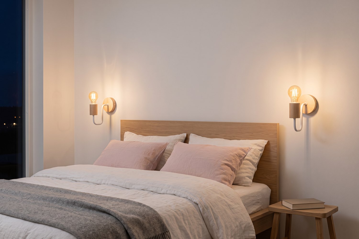 Chambre scandinave la nuit avec deux appliques murales en bois et métal blanc allumées de chaque côté d'un lit en bois clair, linge de lit en lin blanc et rose poudré