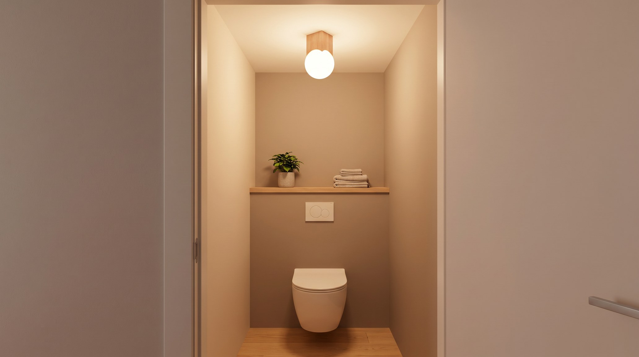 Toilettes étroites le soir, plafonnier japandi composé d'un cube de bois clair et d'un globe en verre opalin allumé en lumière chaude, au-dessus d'une cuvette suspendue blanche, d'une étagère en chêne avec une plante verte et des serviettes en lin, murs beige et taupe